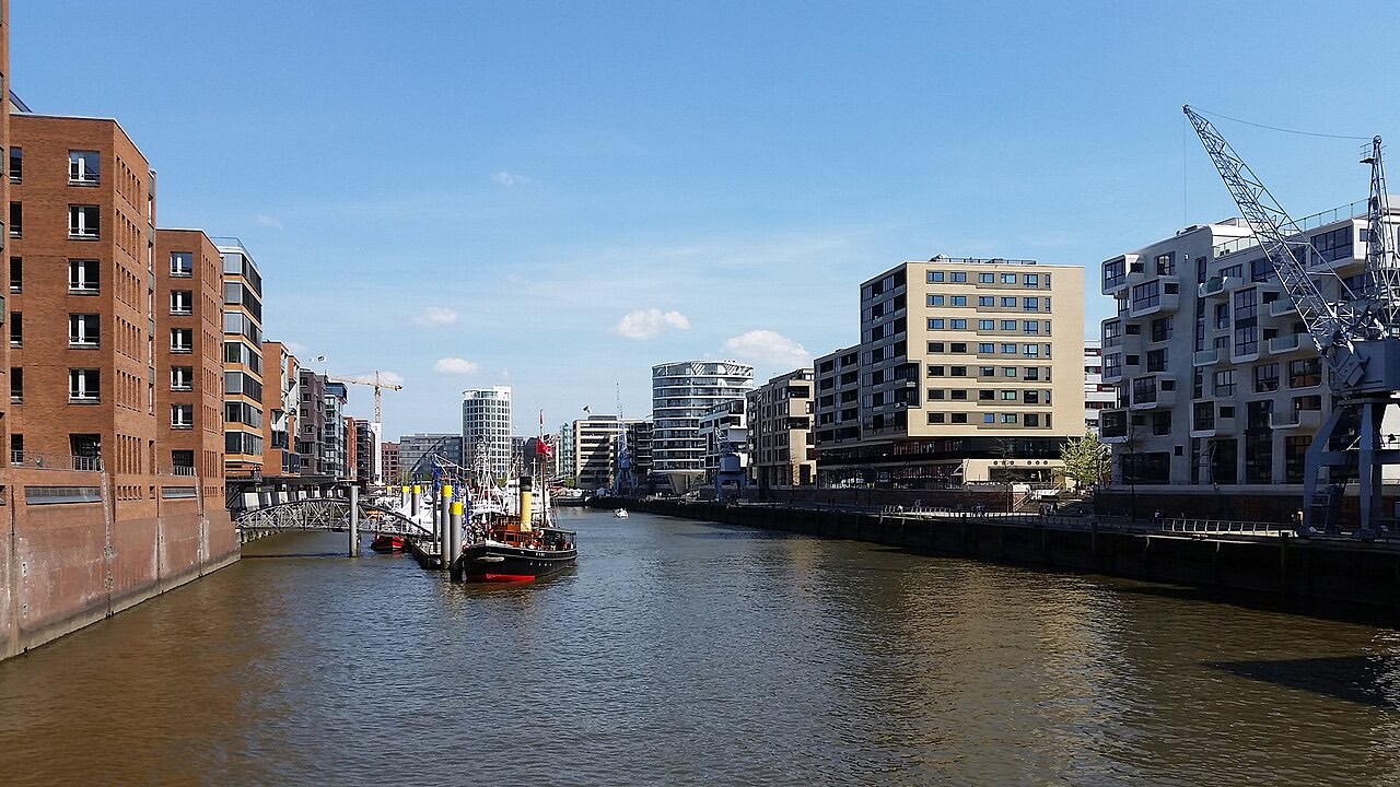 Backsteinspeicher und moderne HafenCity-Architektur entlang eines Hafenbeckens in Hamburg mit altem Dampfschlepper und Hafenkran
